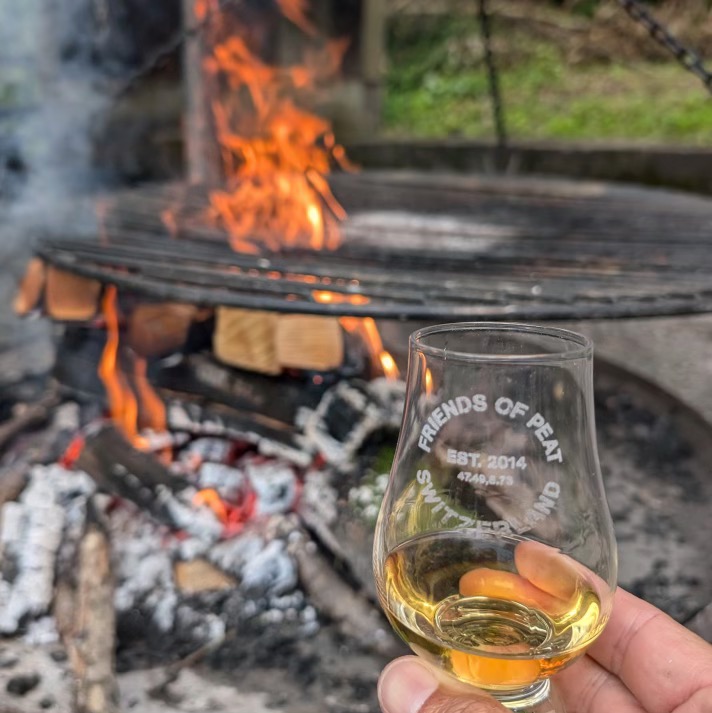 Ein Glas heller Whisky vor einem lodernden Feuer.